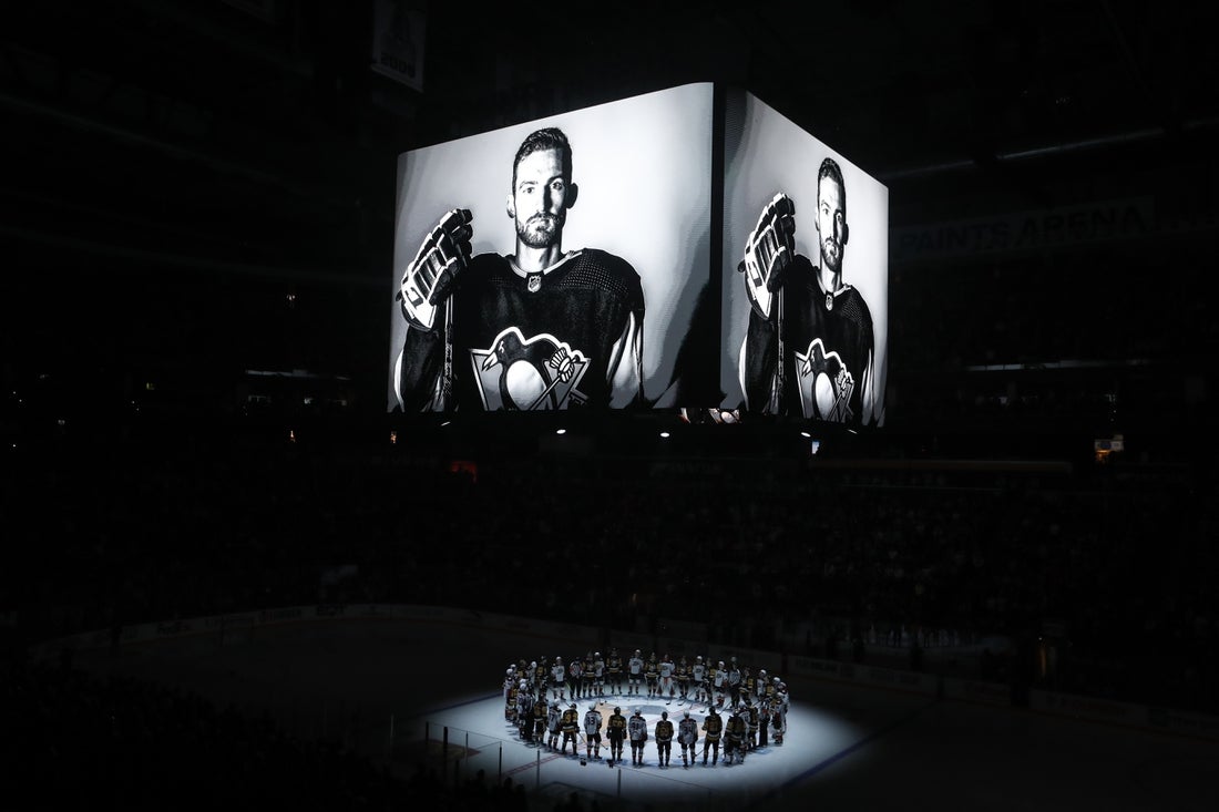 Oct 30, 2023; Pittsburgh, Pennsylvania, USA; Members of the Anaheim Ducks and the Pittsburgh Penguins stand at center ice for a moment of silence at the PPG Paints Arena to honor former Penguin forward Adam Johnson (on scoreboard) who was tragically killed in a hockey related accident in Europe. Mandatory Credit: Charles LeClaire-Imagn Images