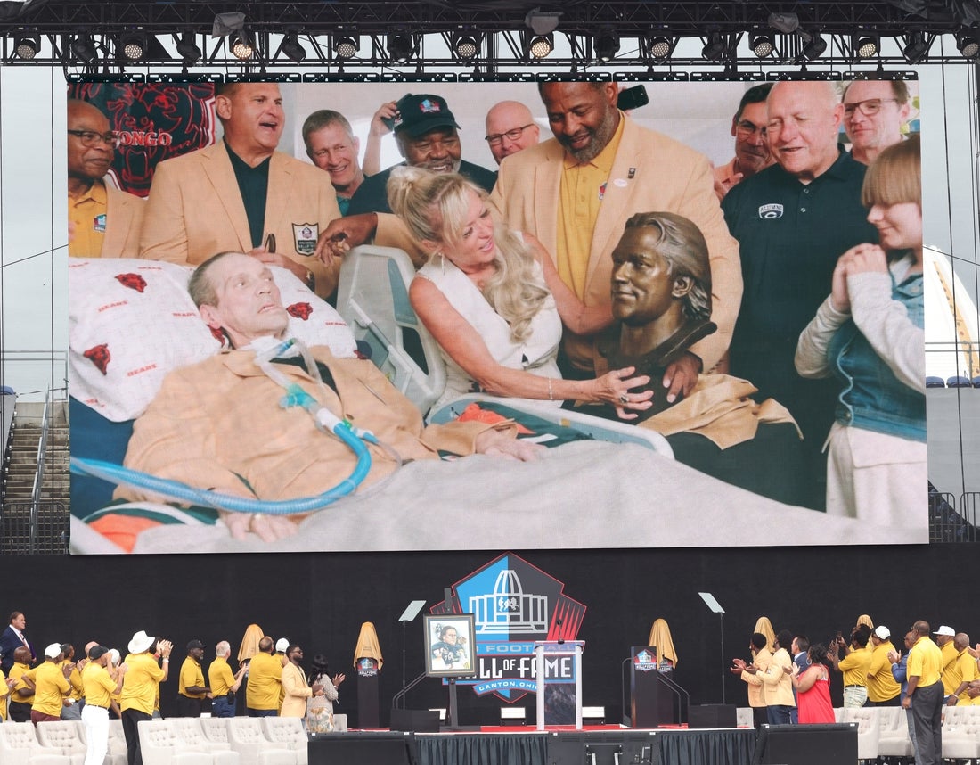 Chicago Bear Steve McMichael and his wife, Misty, unveil his bust at their Chicago home with former teammates during a video unveiling at the Pro Football Hall of Fame on Saturday, Aug. 3, 2024, in Canton, Ohio, at Tom Benson Hall of Fame Stadium.